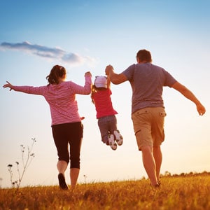A family running in a field at sunset, showcasing parental responsibility. - The Law Offices of Eve McClurg, PA.
