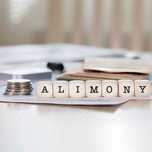 A judge and a lawyer at a table with money, a wedding ring, and a gavel, symbolizing alimony - The Law Offices of Eve McClurg