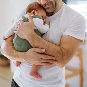 A man gently cradles a baby in his arms, symbolizing the essence of fatherhood and paternity in Florida. - The Law Offices of Eve McClurg, PA